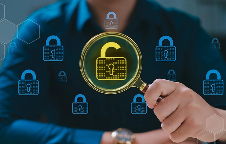 A magnifying glass with a bright yellow lock icon with its shackle open is held up in the center of the image. The magnifying glass is held by a person in a blue shirt with the sleeves rolled up. All around the magnifying glass are blue, closed lock icons. The background is a blurry office setting.